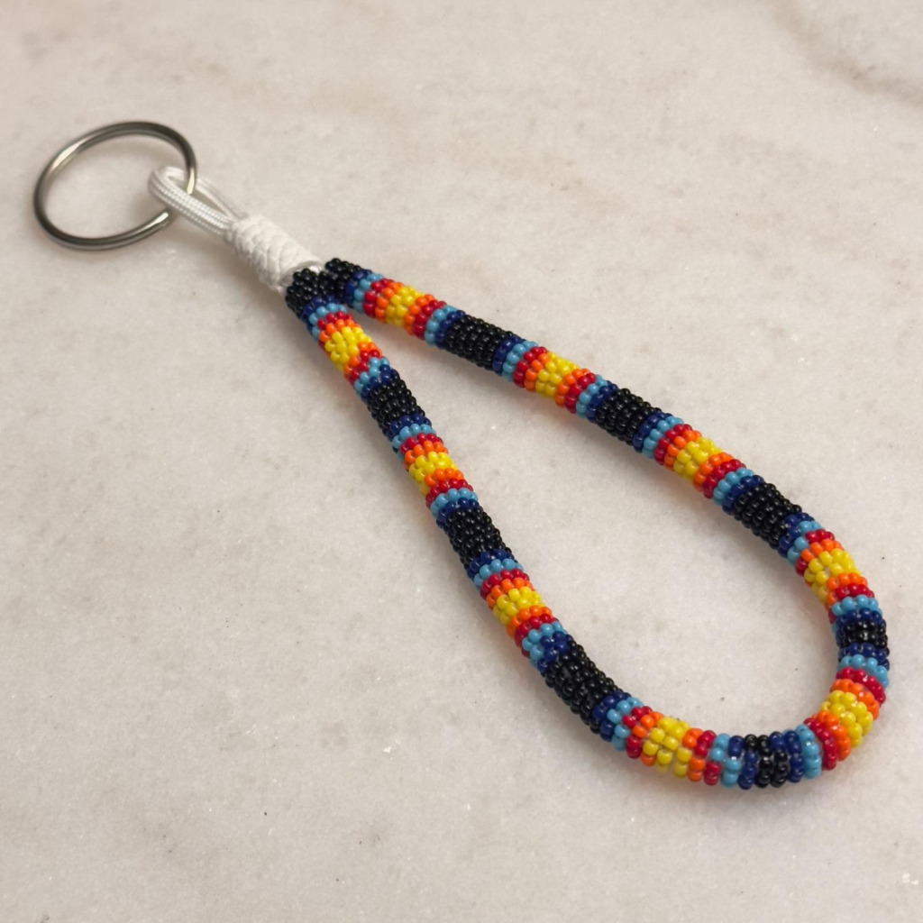 A black, blue, red, orange, and yellow bead wrapped wristlet keychain on a marble background