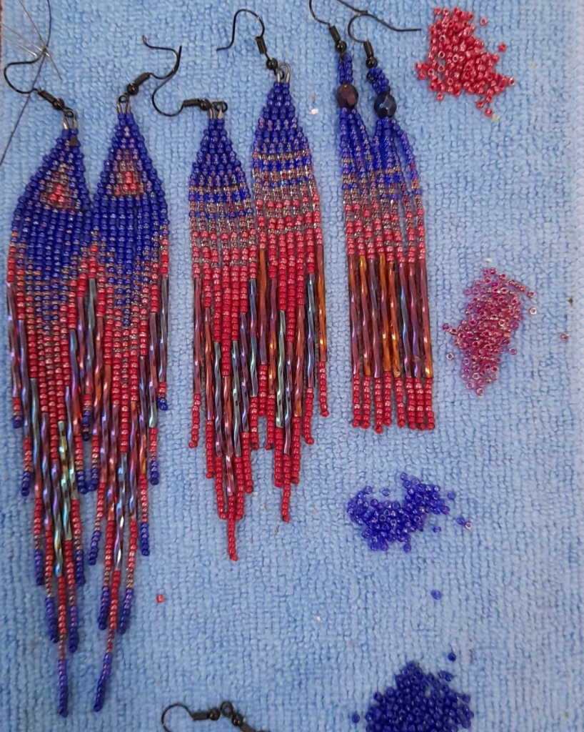 Three pairs of dark blue and dark red beaded earrings with black findings on a blue background.