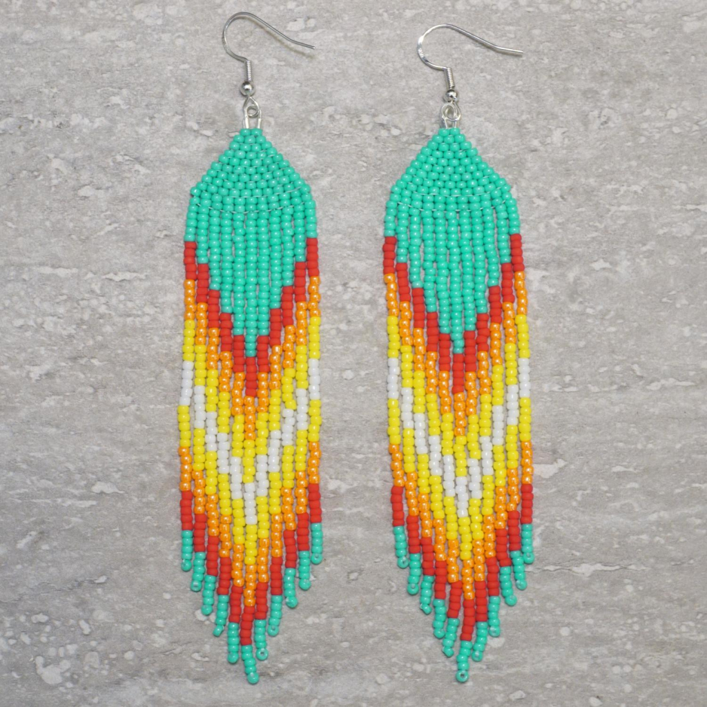 A pair of turquoise, red, orange, yellow, and white beaded fringe earrings on a stone background