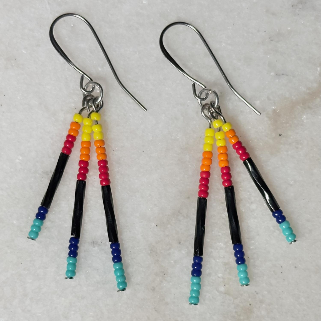 A pair of yellow, orange, red, black, and blue beaded drop earrings on a marble background