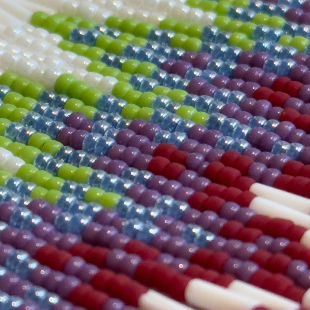 A super close up picture of three beaded fringe earrings next to each other. The beads are pearl white, apple green, blue, purple, and matte dark red.