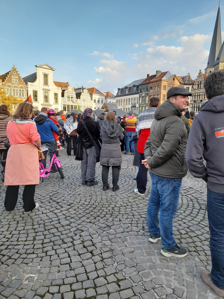 Een hel grote groep mensen, Palestijnse vlaggen, een podium met sprekers op de Gentse Vijdagmarkt. Ongeveer de halve Markt staat vil.