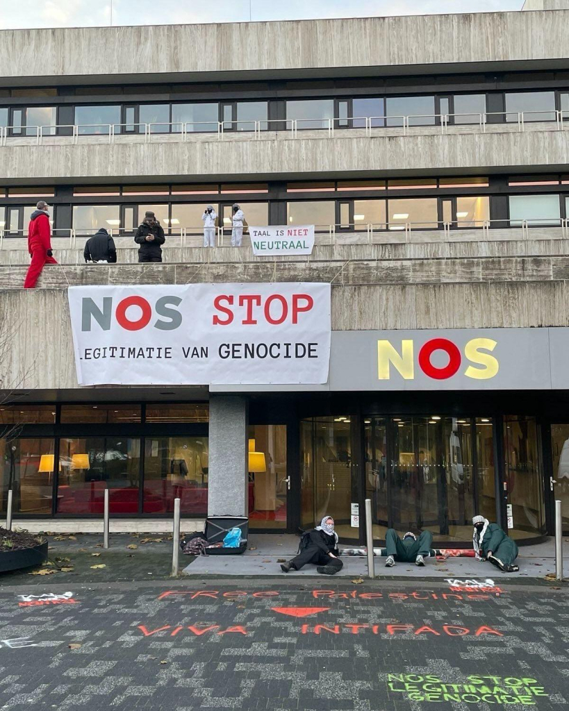 Foto van het NOS-gebouw met activisten op het balkon en voor de ingang. Twee banners met de teksten: 'TAAL IS NIET NEUTRAAL' en 'NOS STOP LEGITIMATIE GENOCIDE'. 