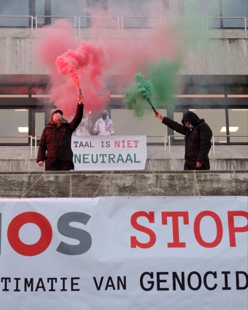 Foto van het NOS-gebouw met activisten op het balkon met flared. Twee banners met de teksten: 'TAAL IS NIET NEUTRAAL' en 'NOS STOP LEGITIMATIE GENOCIDE'. 