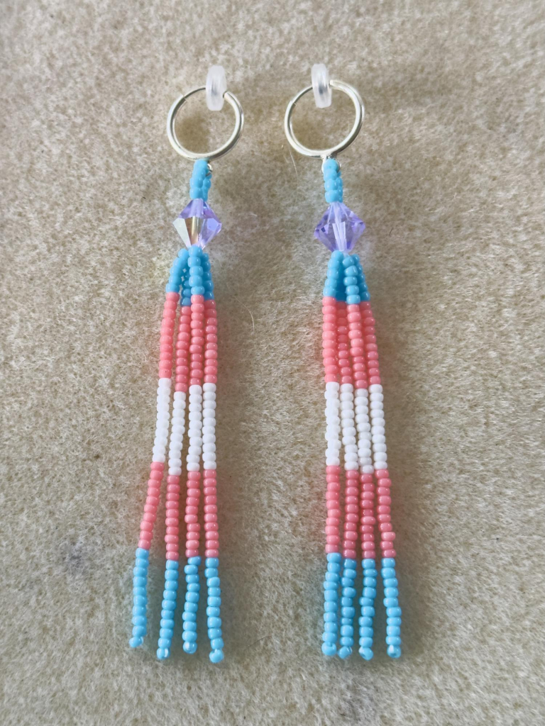 A pair of beaded trans pride dangles with silver clip-on hoop findings on a bead mat 