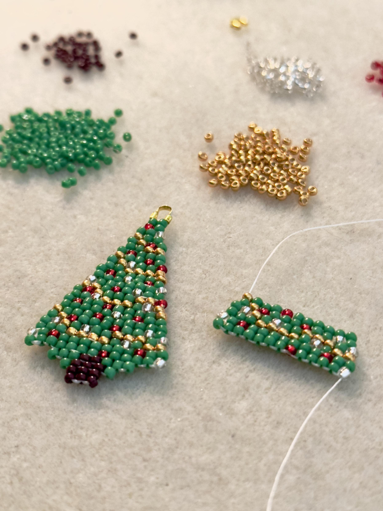 A pair of Christmas tree beaded earrings in progress on a bead mat