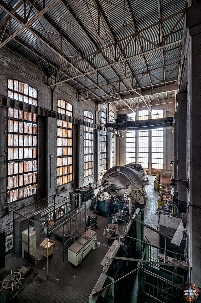 View of a three story turbine hall from above. In the center is a large turbine in front of high banks of windows along the walls.