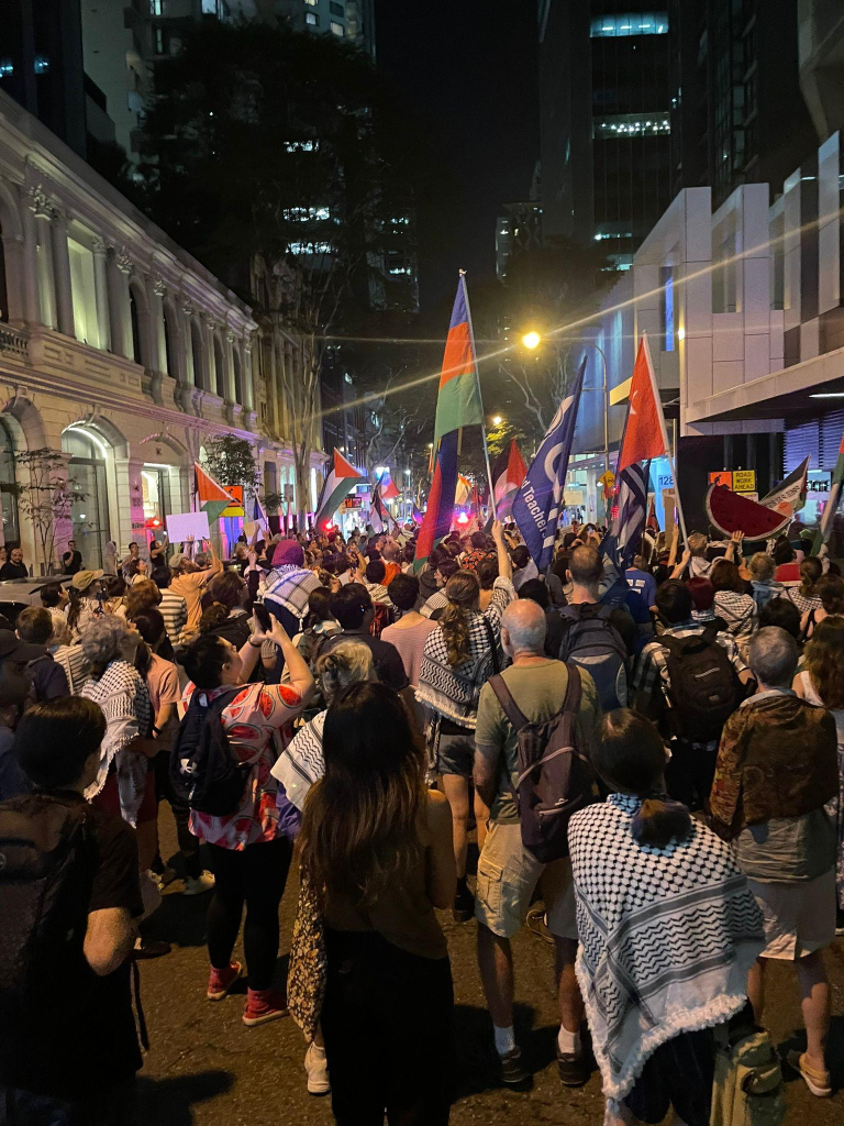 A large crowd marches through the streets of Magandjin with Palestinian flags and wearing kuffiyeh and watermelon shirts