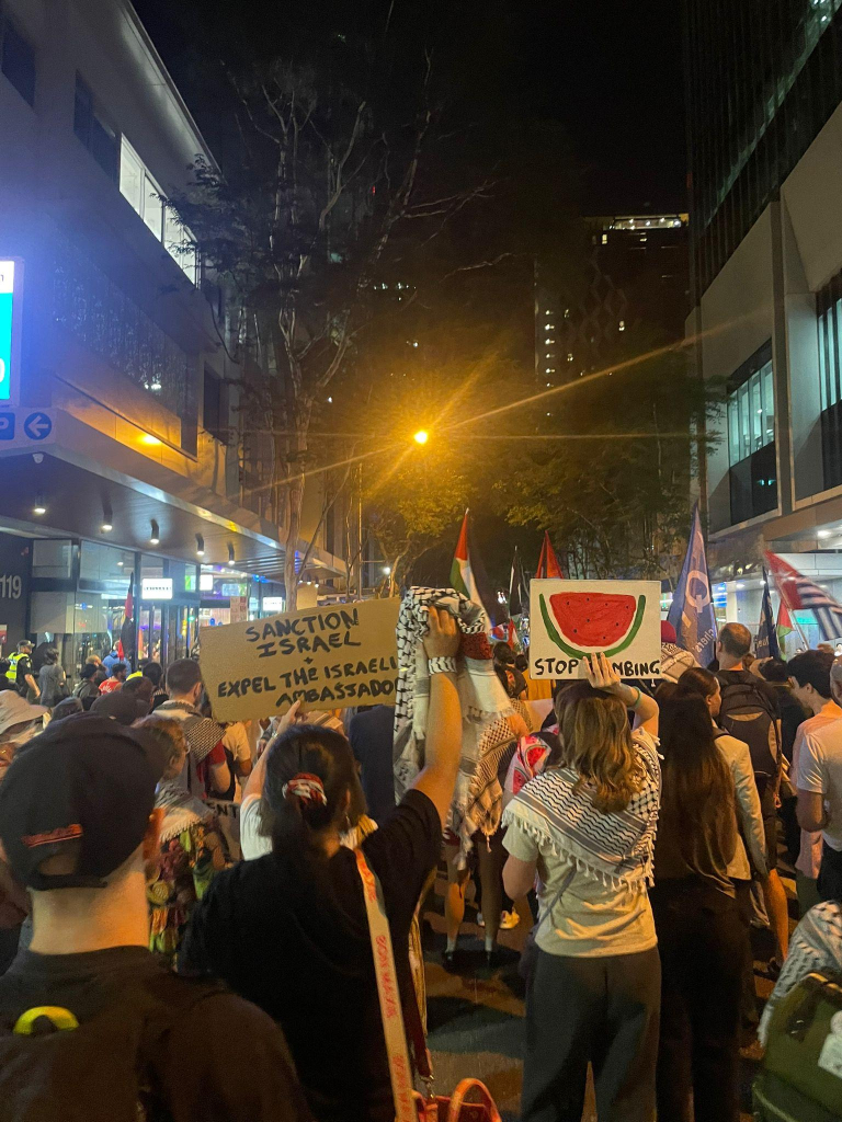 A marching crowd with signs that read "sanction Israel, expel the Israeli ambassador" and "stop the bombing"