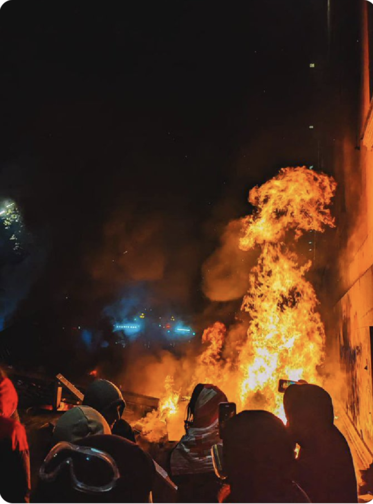 Protestors in Georgia face off against the police with a barricade between the two groups. The barricade is on fire.