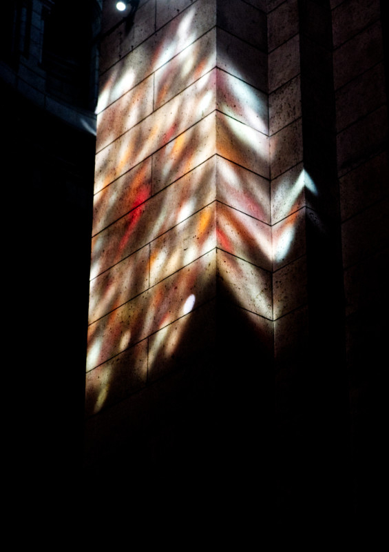 A colour photograph of the interior  of Sacre Coeur cathedral in Paris.

The picture shows a signle stone column illuminated by the light from a stained glass window, dappling the column with white, orange and red light.

Aside from the obliquely illuminated column, the interior is in deep, dark shadow, with no other details visible.