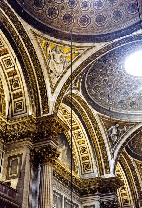 A colour photographs in portrait orientation showing the ceiling the church of the Madelaine in Paris and the supporting arches and coloums, all heavily decorated in the baroque style.