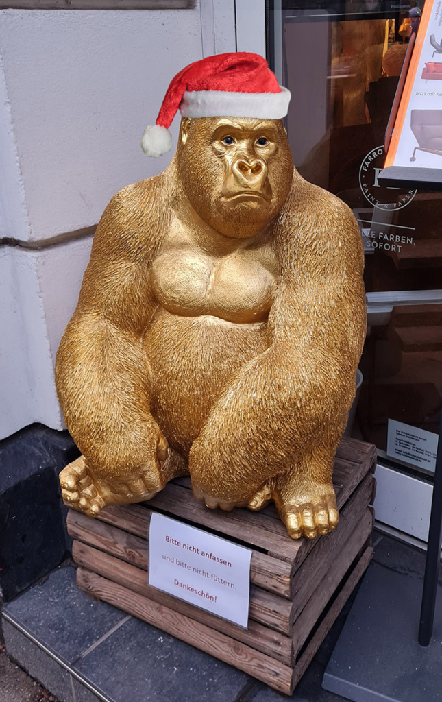 A big golden gorilla scupture sitting in front of a shop entrance, wearing a Santa hat.