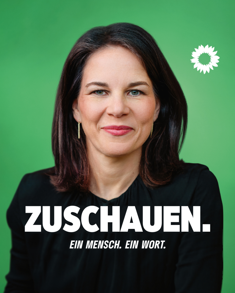 Ein Wahlplakat mit grünem Hintergrund und einer weißen Sonnenblume oben rechts. Im Hintergrund Annalena Baerbock, der in die Kamera blickt. Davor ein Schriftzug "Zuschauen.", darunter ein kleiner Untertitel: "Ein Mensch. Ein Wort."