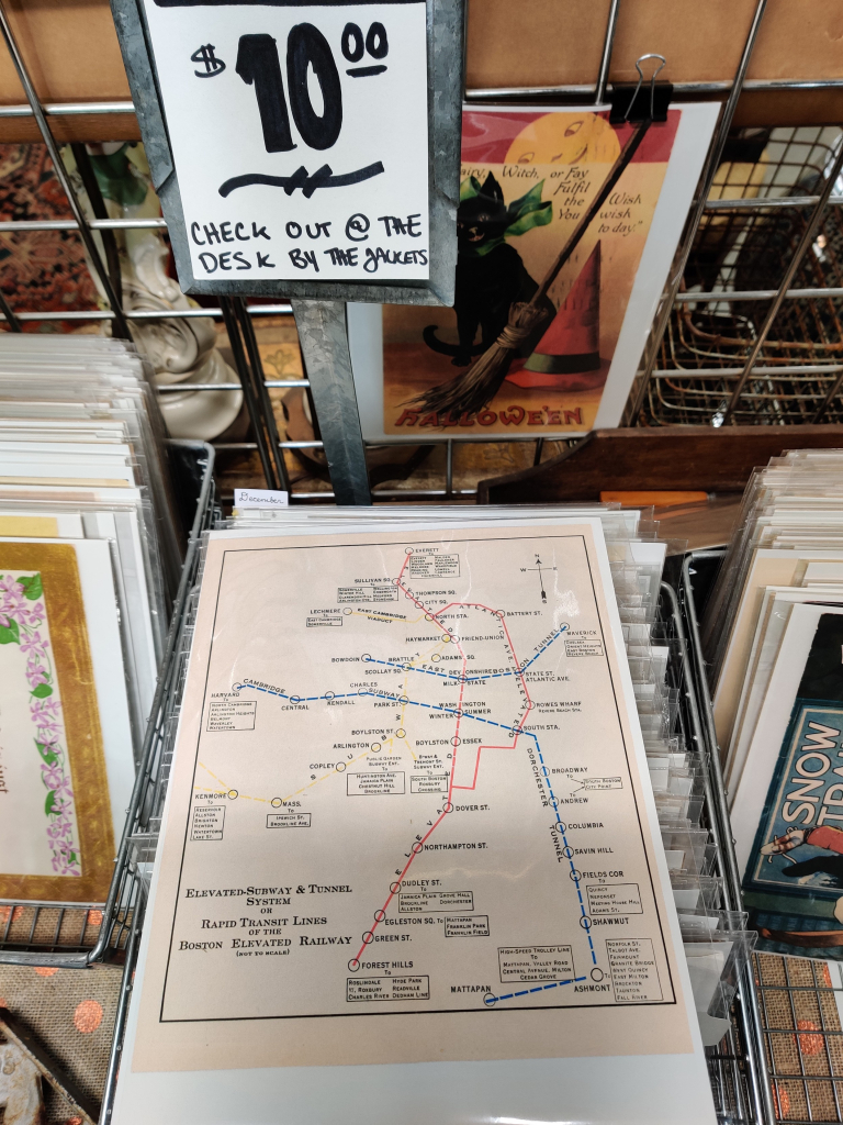 photo of a price sign with black lettering ($10 check out @ the desk by the jackets) above a print of train stop names along multi-colored lines