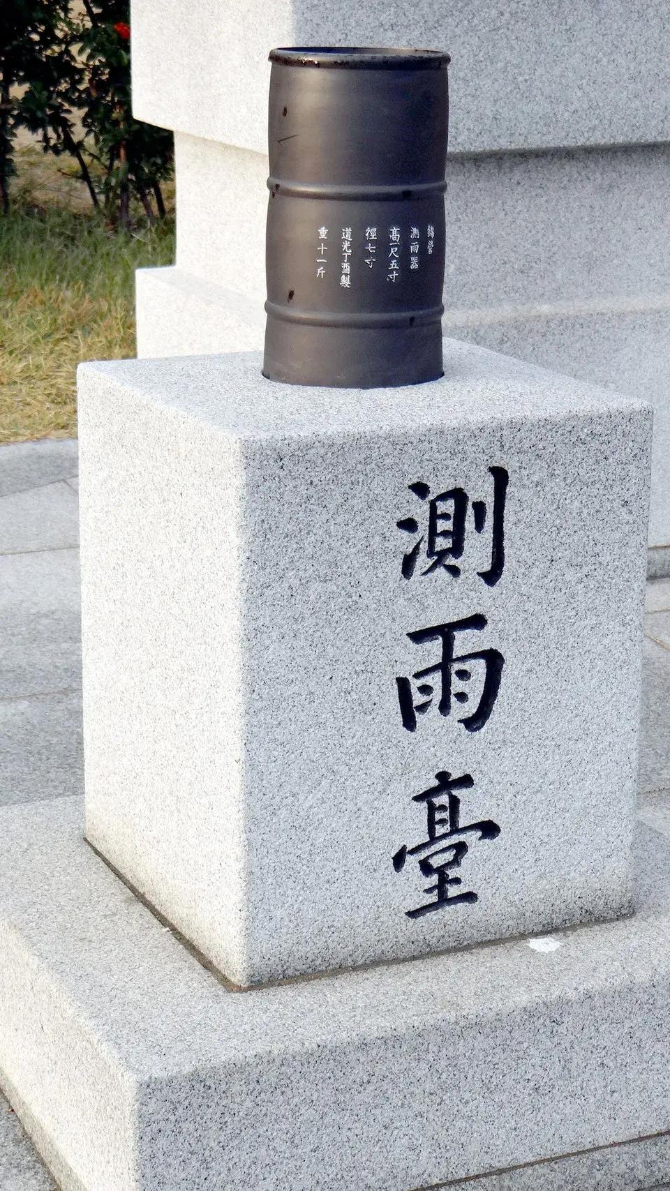 The image features a stone pedestal with inscriptions in what appears to be Chinese characters, and on top of it is a cylindrical container, likely made of metal. The pedestal and container might be part of a monument or a rain gauge, given the context of the inscriptions, which seem to relate to measuring rain. This setup typically indicates a meteorological or environmental theme.

Image Credits: Wikimedia / Steve46814 / CC BY-SA 3.0