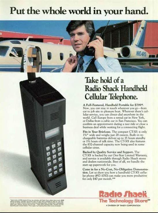 Vintage advertisement for a Radio Shack Handheld Cellular Telephone. The ad features a person using the phone in front of an airplane, with the headline "Put the whole world in your hand." The phone is described as a full-featured, handheld portable device priced at $799.99. It highlights features such as direct-dial anywhere in the world, compact size, and a battery life of up to 15 hours standby or 1.7 hours talk time. The ad also mentions a one-year limited warranty and a no-cost demonstration offer. The Radio Shack logo and slogan "The Technology Store" are at the bottom