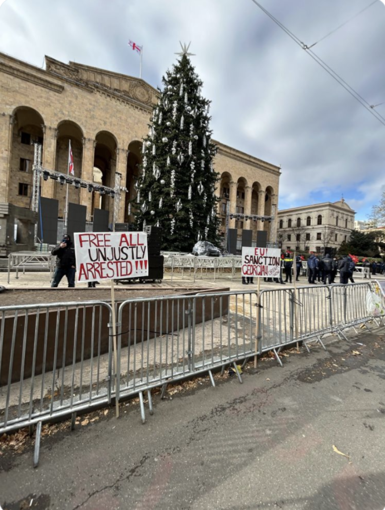 Christmas tree outside parliament in Tbilisi Georgia. There is a stage set for the opening ceremony with protest signs all around it. One says 'Free all unjustly arrested.