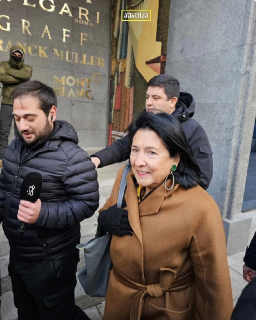 President Salome Zourabichvilli walks outside parliament in Tbilisi, Georgia. She has a few bodyguards and is being interviewed by a journalist. 