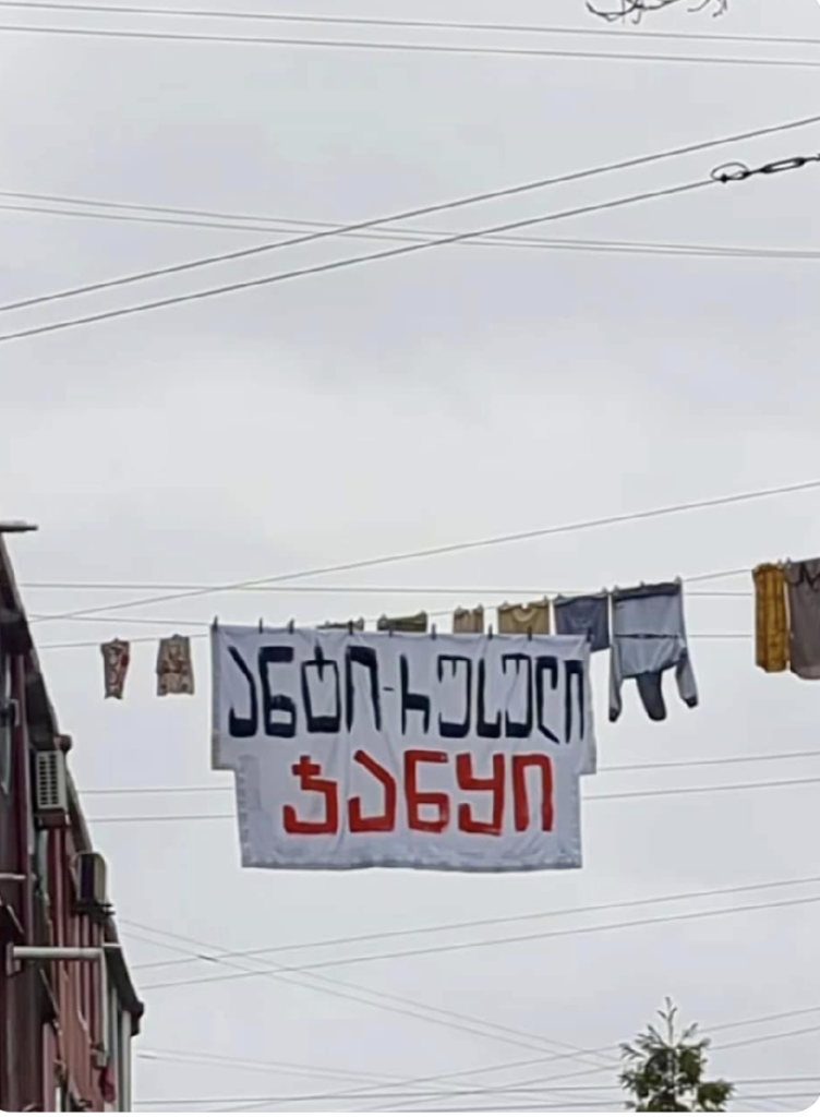 A white sheet is hung on a washing line between buildings in Batumi, Georgia along with other clothes. it says in Georgian 'Anti Russian Uprising.