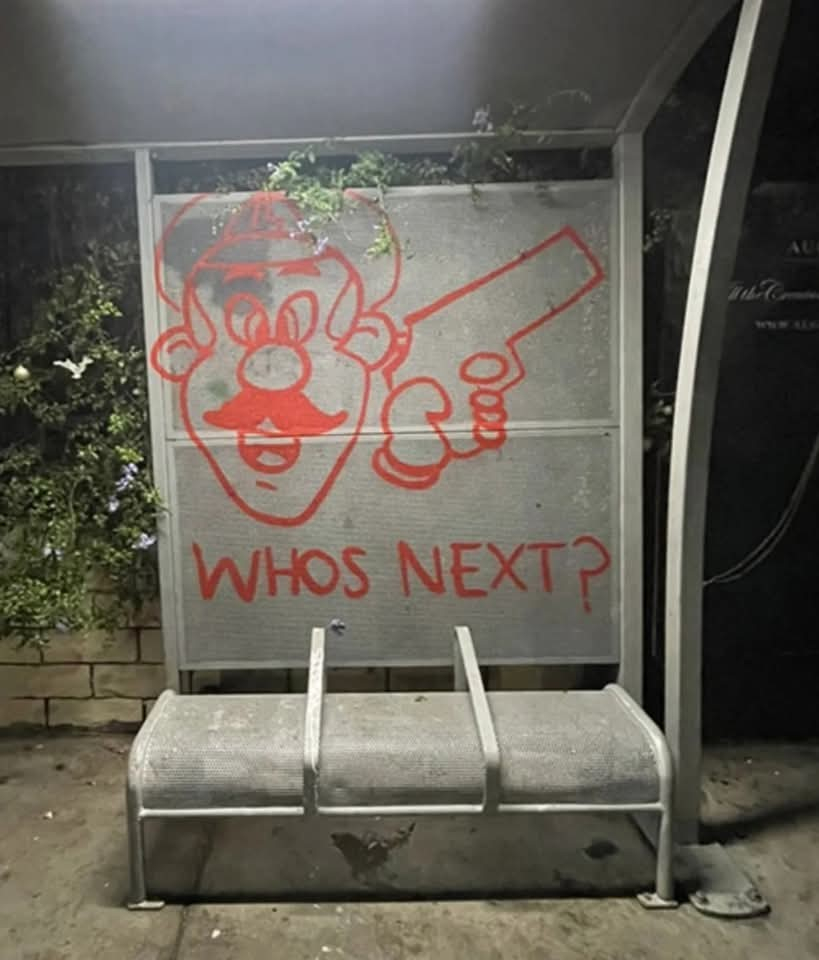 Graffiti on a wall showing a cartoon character with a gun saying Who's Next?