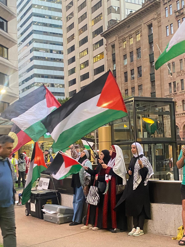 A group of young girls wearing traditional Palestinian outfits and kuffiyeh and waving Palestinian flags