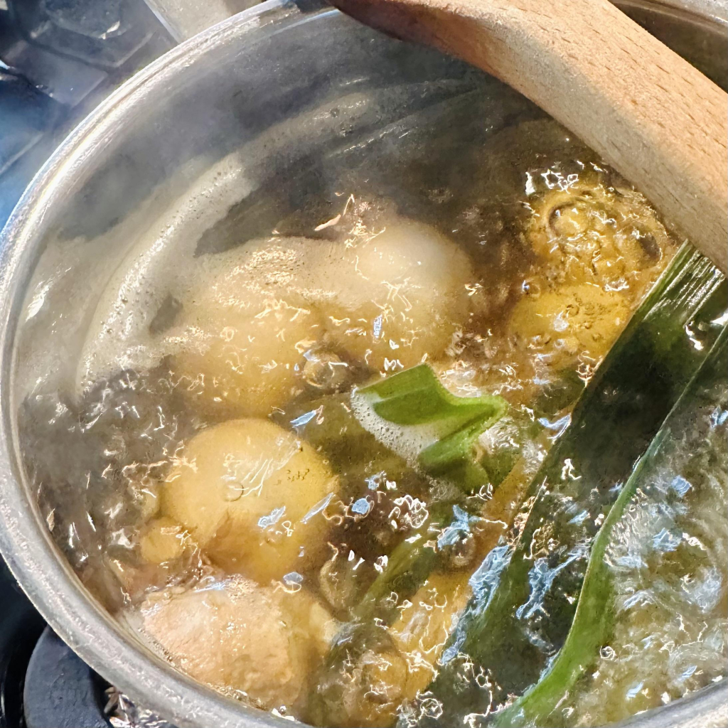 A photo of rice balls in a lot with brown sugar and ginger and pandan leaves