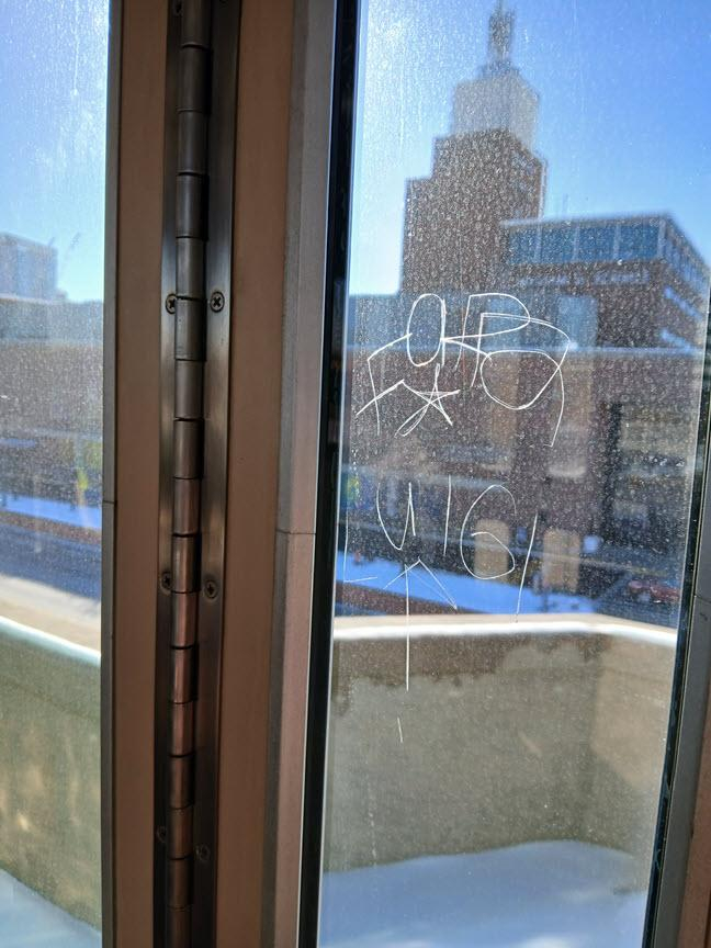 One of the windows from a Boston Green Line train door. Etched into the glass is the text:
"For Luigi" with a star in the center and an upward pointing arrow.

In the background the Museum of Science is visible but blurry, and the window is a little grungy. But I think the message is clear. 