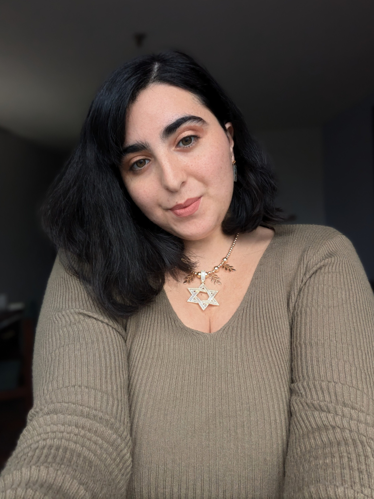 Selfie of me, I have dark brown hair and army green sweater and I'm wearing a golden Magen David large necklace with golden leaf pendants