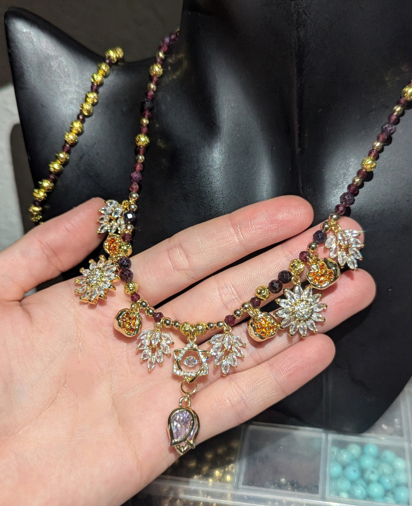 A necklace with Garnet gemstones, golden Magen David with zirconia leaves, flowers and pomegranate pendants