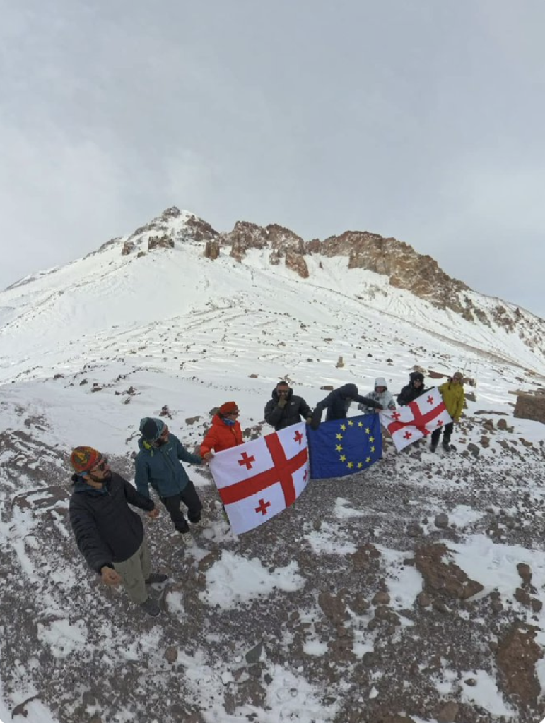 Mountaineers in Georgia form a human chain on top of a mountain in Georgia with Georgia and EU flags.