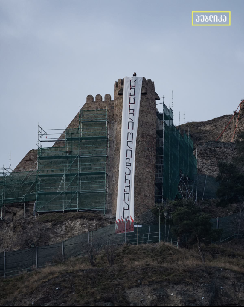 Huge  vertical protest banner on Narkala Fortress wall in Tbilisi, Georgia. It says Fire to Oligarchy in Georgian with flames at the bottom.