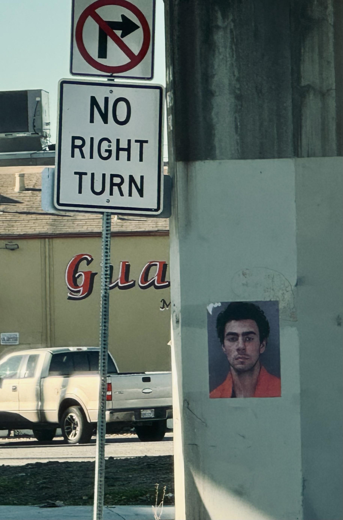 Street scene with No Right Turn sign and support column with small artwork featuring Luigi Mangione’s face