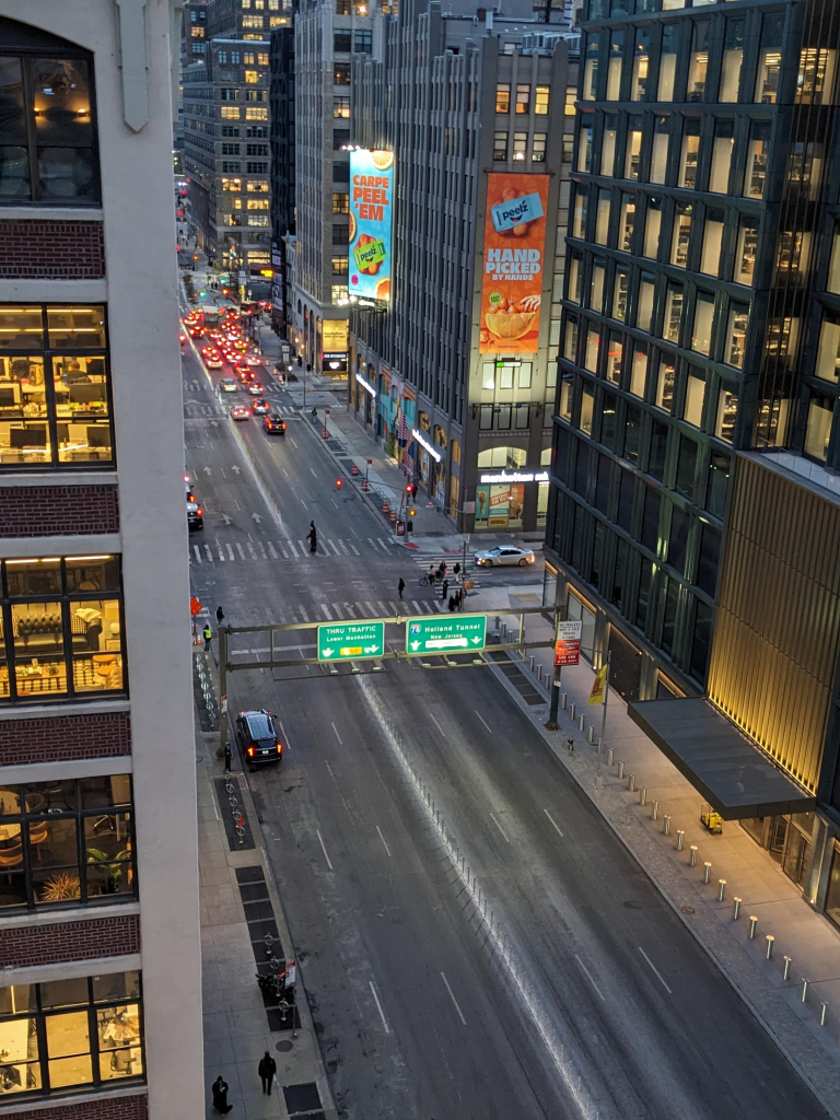 A photo of Varick Street in Manhattan taken from my office window, looking downtown towards the Holland Tunnel entrance three blocks away, shortly before sunset. There are a few cars waiting at a red light on the block closest to the tunnel, but the rest of the street is empty of cars. 