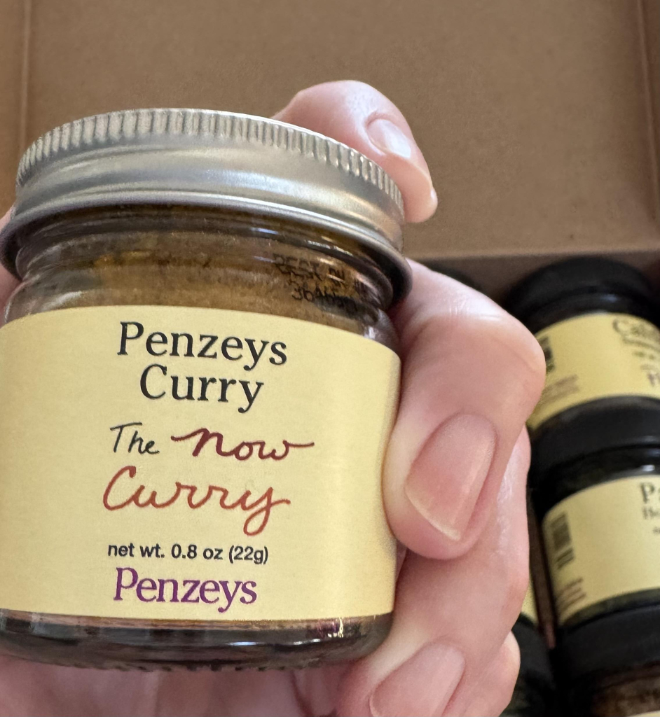 A close up of a hand holding a jar of Penzeys Curry spice. 