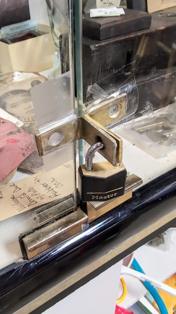 A picture of a display case with a lock on it. But the lock is a Master lock. And the hardware that the Master lock is locking together isn't actually mounted to the display case, it's just taped on with clear Scotch tape.