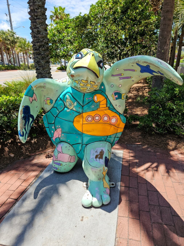 One of the few remaining big sea turtle sculptures/statues around Jacksonville. Part of a charity project and after a period of time most were removed, much like the Sea Cows and Jaguars. A big, green, happy sea turtle with outstretched upper floggers, standing on hind legs, as if to embrace. Tourists take photos between the flippers. Mostly shades of green, but also colorful seaside images added in bright colors, like a yellow submarine.