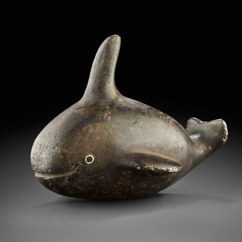 official museum photo, side profile on gradient black-grey background; brownish-grey steatite (soapstone) carving in the form of a plump whale with a tall top fin, small beady eye, and carved smile…very cute!!