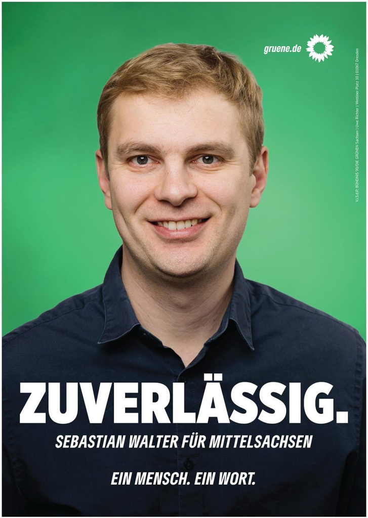 Freundlich blickender, offen lachender junger männlicher Mensch mit kurzem Haar und dunklem Hemd vor grünem Hintergrund. 
Schriftzug: Zuverlässig. Sebastian Walter für Mittelsachsen. Ein Mensch. Ein Wort.