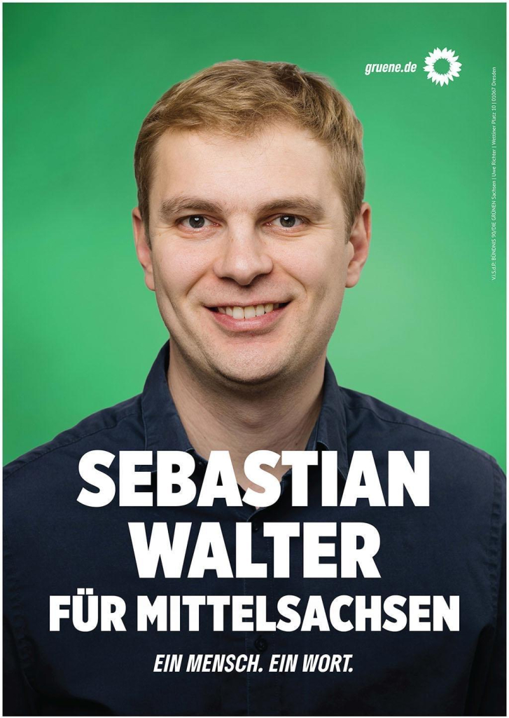 Freundlich blickender, offen lachender junger männlicher Mensch mit kurzem Haar und dunklem Hemd vor grünem Hintergrund. 
Schriftzug: Sebastian Walter für Mittelsachsen. Ein Mensch. Ein Wort.