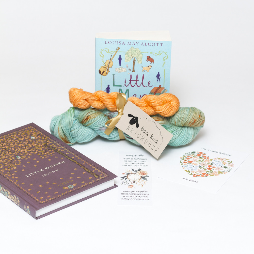 Picture shows a sock set of yarn consisting of a main skein which is aqua with orange, purple and green speckles and a mini skein which is orange. They are tied together with gold ribbon. Behind the yarn stood on its end is a copy of Little Men by Louisa May Alcott. The book is aqua with purple and green drawn images on it. In front of the yarn is a notebook, a bookmark and a postcard.