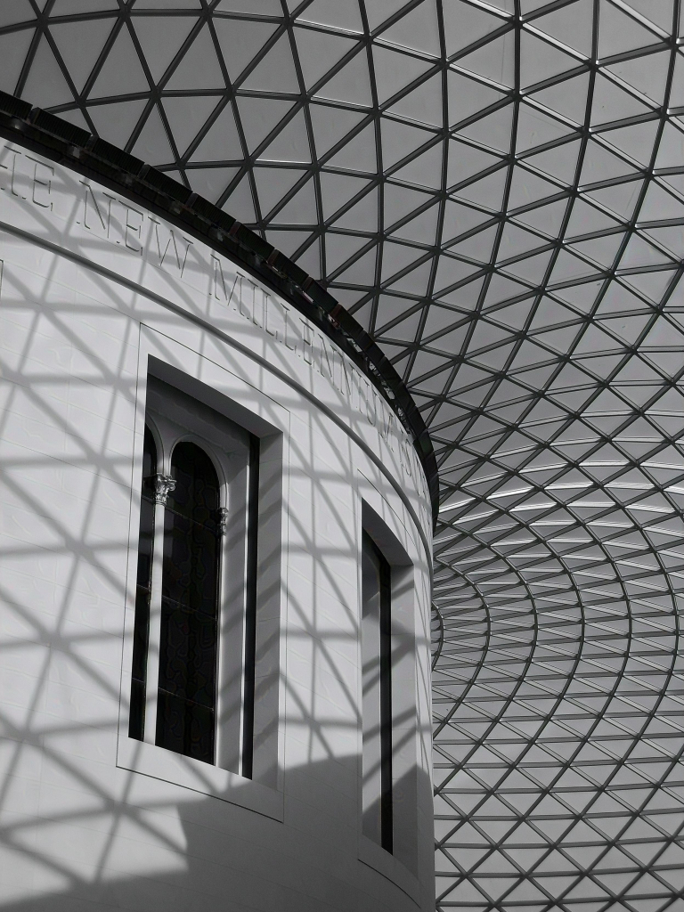 Black and white photo of a portion of a cylindrical structure, the top edge of which supports an expansive glass and metal roof