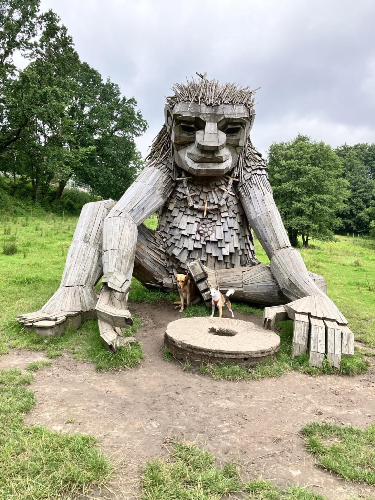 Ein riesiger Troll aus Holz sitzt hinter einem Mühlstein (in Dänemark)
