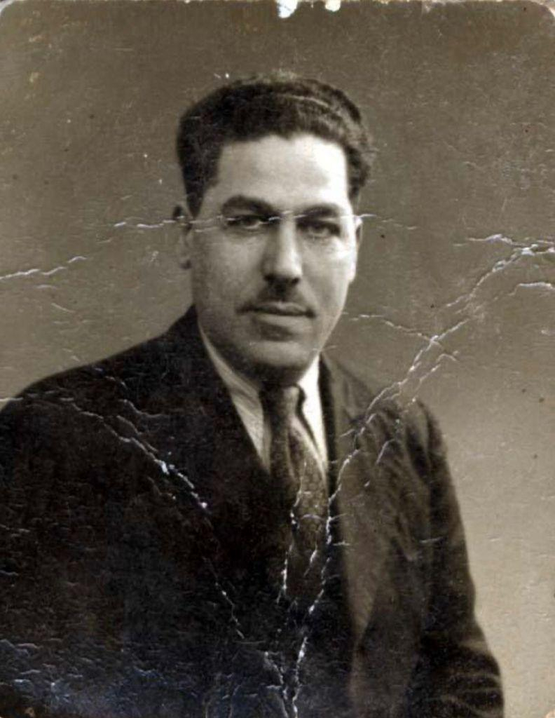 Portrait photograph of a mature man. Photographed against a solid background. He is wearing a jacket, white shirt and tie. He has dark short hair. He is looking straight into the lens.