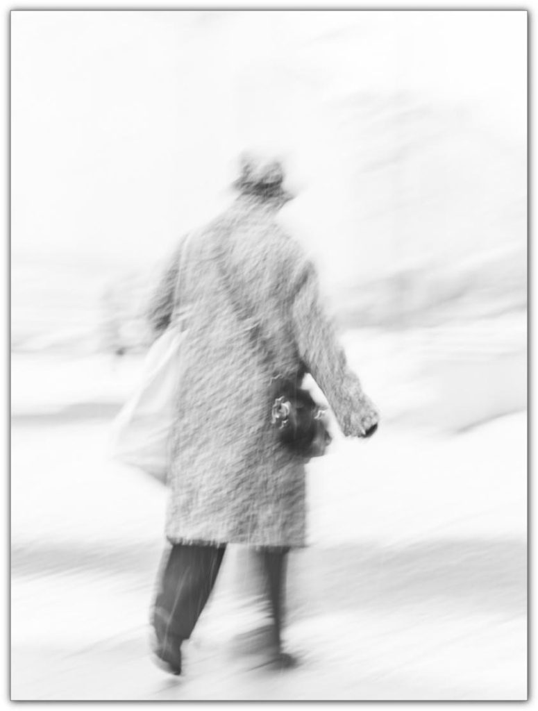 Eine ältere Frau läuft durch eine verschneite Fußgängerzone. Das Foto ist durch Bewegung der Kamera leicht verschwommen.

An elderly woman walks through a snow-covered pedestrian zone. The photo is slightly blurred due to camera movement.