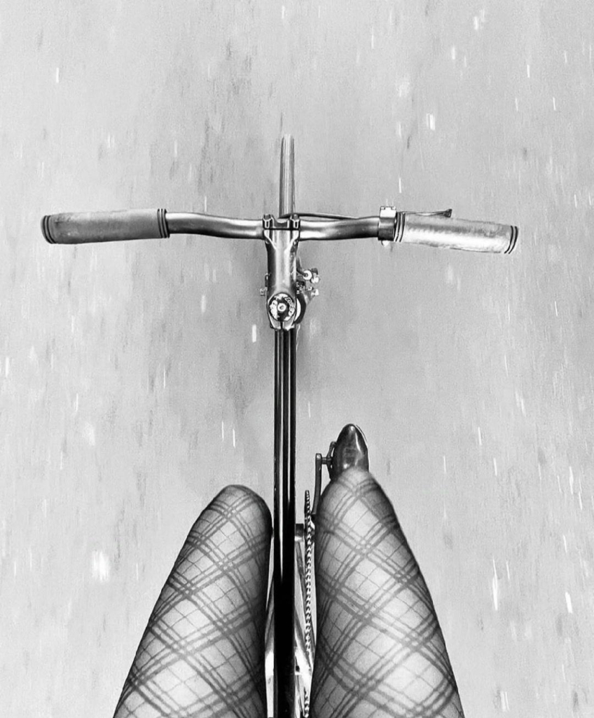 Photography. A black and white photo of a cyclist, taken from above. The photo shows only the legs in fishnet stockings of a person on a bicycle. The view goes from the legs to the bicycle handlebars, the hands are not visible. The person, presumably female, is riding freehand on a road. The photo conveys a sense of speed, self-determination and freedom.
Info: Unfortunately, research on the artist only revealed her name and the country Mexico. Nothing more is known, although the photo has often won awards.