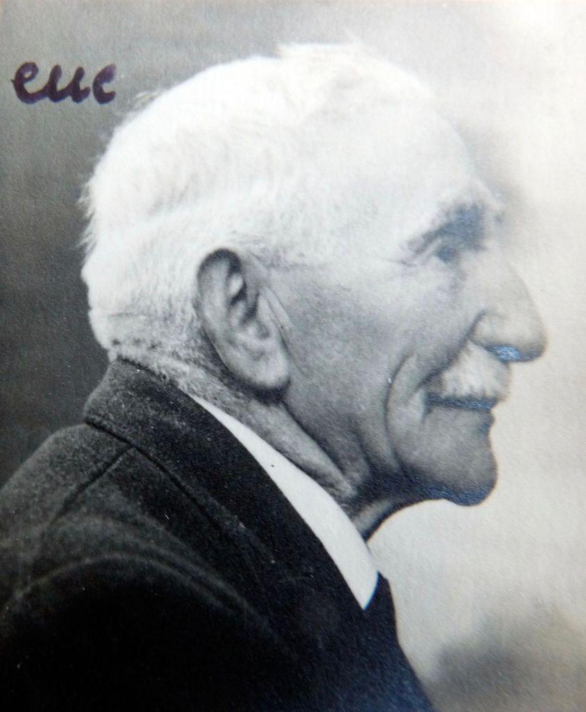 Profile view of an elderly man, with white hair and wearing a dark suit.