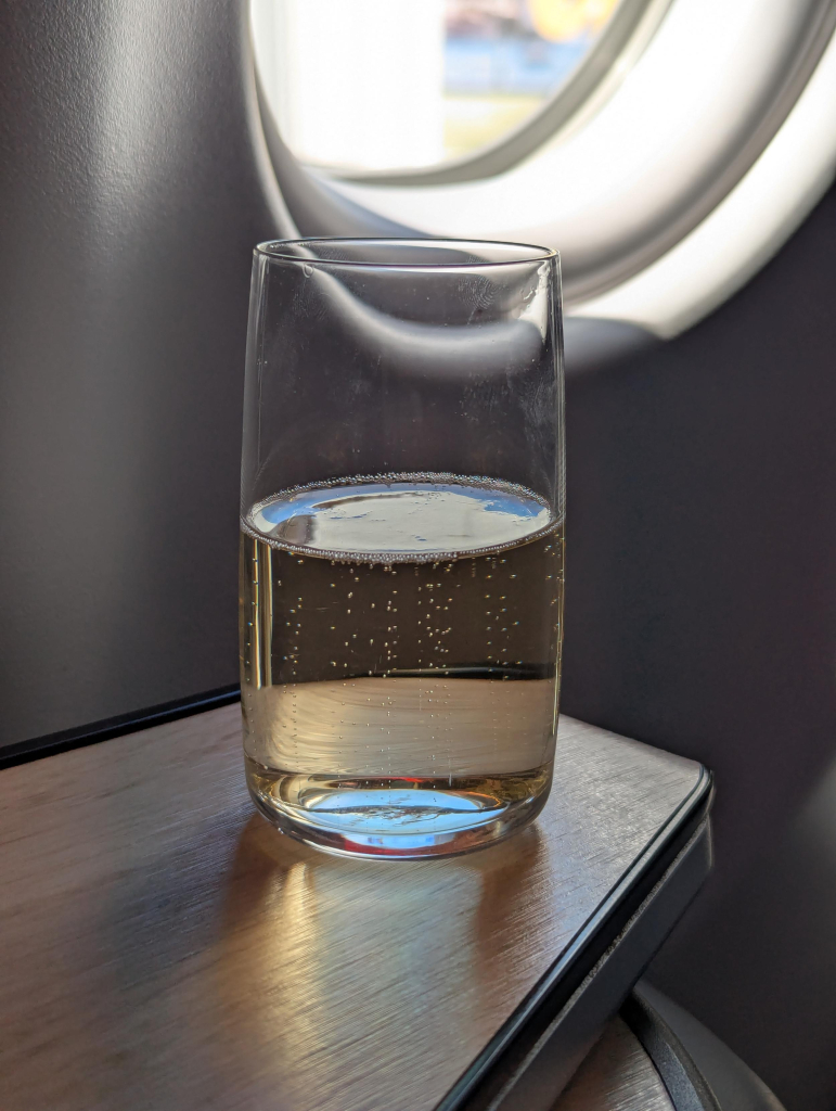 Photo of a small glass of champagne on a side table by an airplane window.