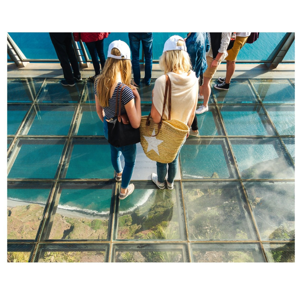 Aussichtsplatform mit Glasboden auf Madeira. Mehrere Personen stehen auf der Platform, einige hundert Meter unter ihnen die Küste und das Meer.