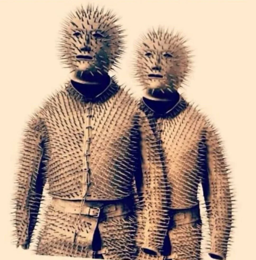 Photograph of two full-body suits and full-head masks are covered in sharp pins. 